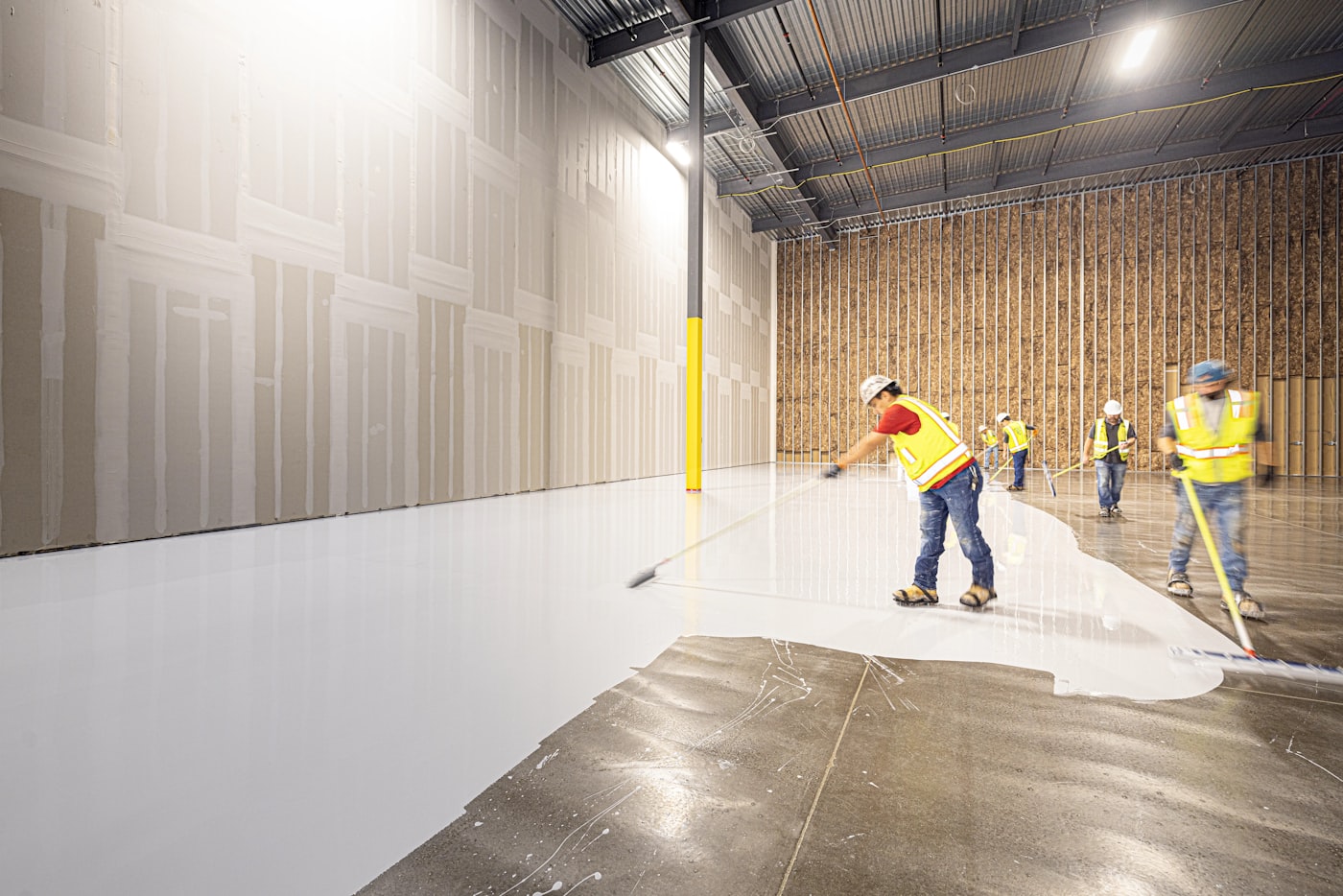 Applicators installing a polyaspartic coating across a large industrial floor.